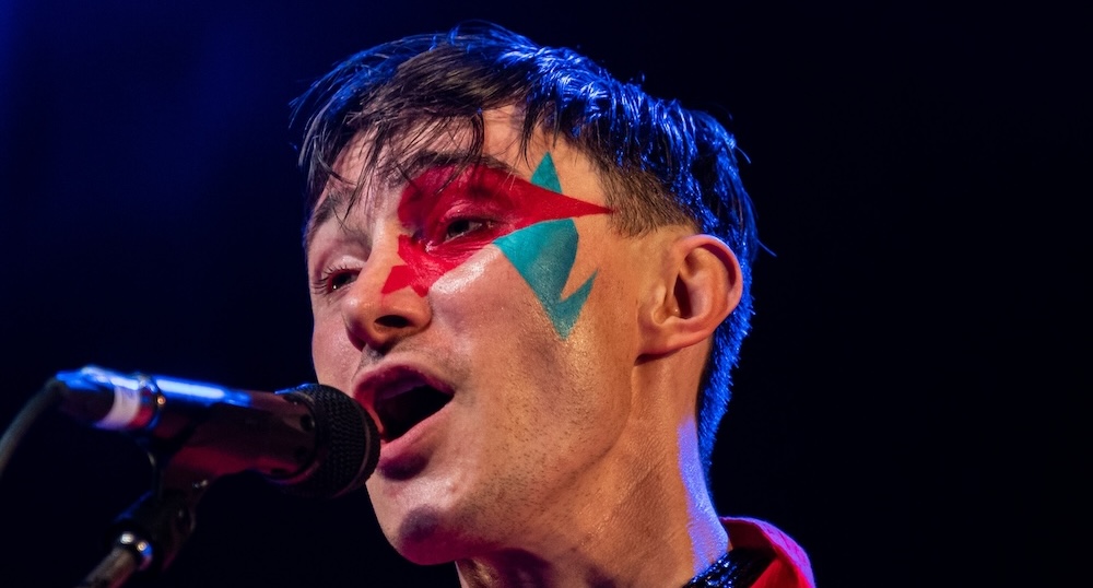 Alex Etchart performing live at Rich Mix in Shoreditch, London, singing into a microphone with Bowie-inspired makeup during La Linea Latin American music festival